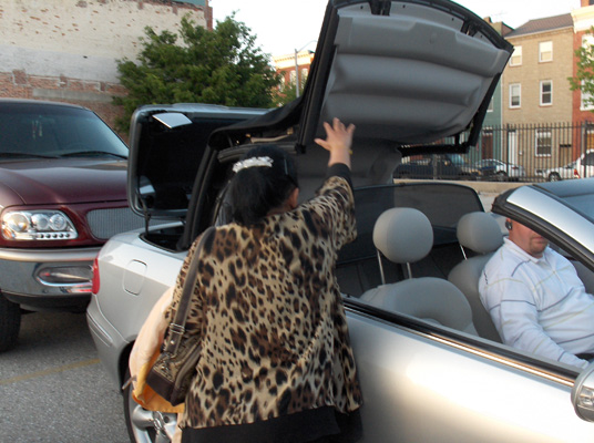 Paul sits in the car while the top of the car is rising up (it is hinged at the back).  Nanta is standing beside the car with her arm extended toward the top (it just went beyond her reach).